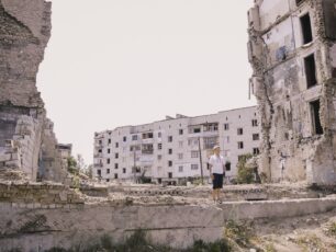 En pojkte står i en sönderbombad byggnad i Ukraina