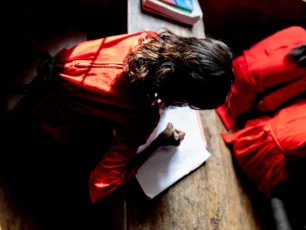 Flicka lutar sig över en skolbänk och skriver i ett block