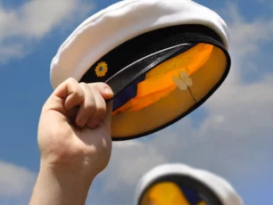 En person som håller i en studenthatt under en molnig blå himmel.