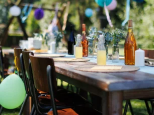 Dukat bord för fest ute i en trädgård en solig sommardag. Bordsdukning med glas, fruktlemonad. Färgglada pappersdekorationer och blombuketter.
