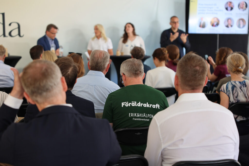 Människor sitter i kyrkbänkarna i Visby, och lyssnar på ett seminarium. En i publiken har en grön t-shirt med texten "Föräldrakraft" på.