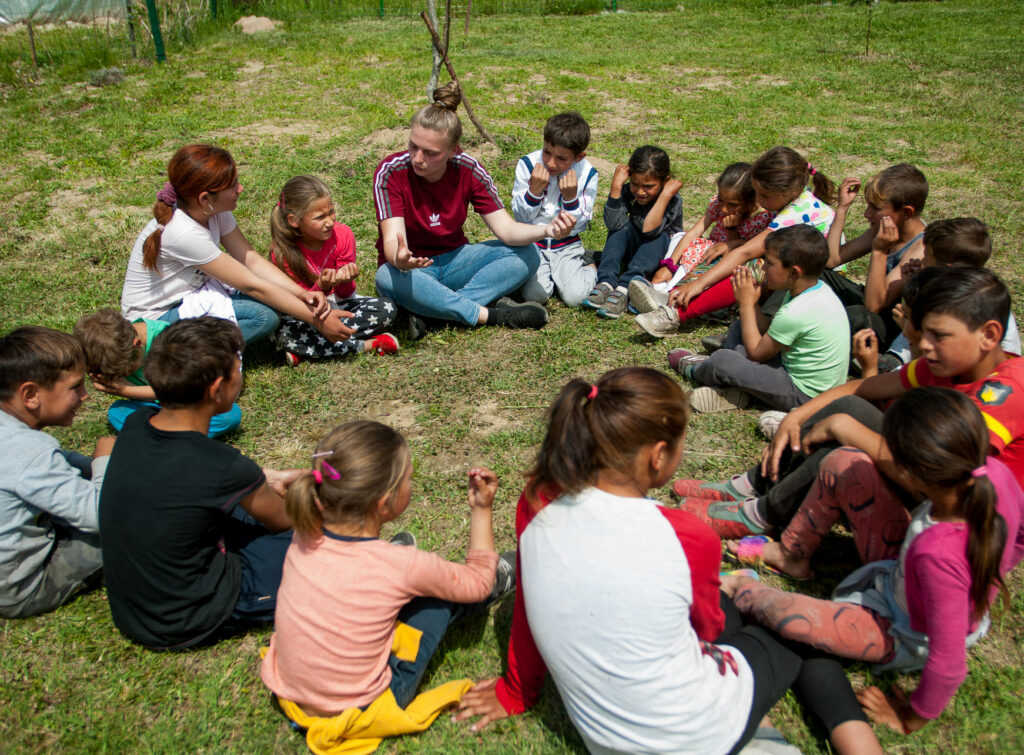 Children are sitting in a circle on a lawn.